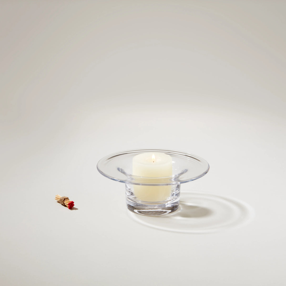 Clear glass hurricane candleholder with wide rim containing a cream-colored pillar candle and a red decorative match.