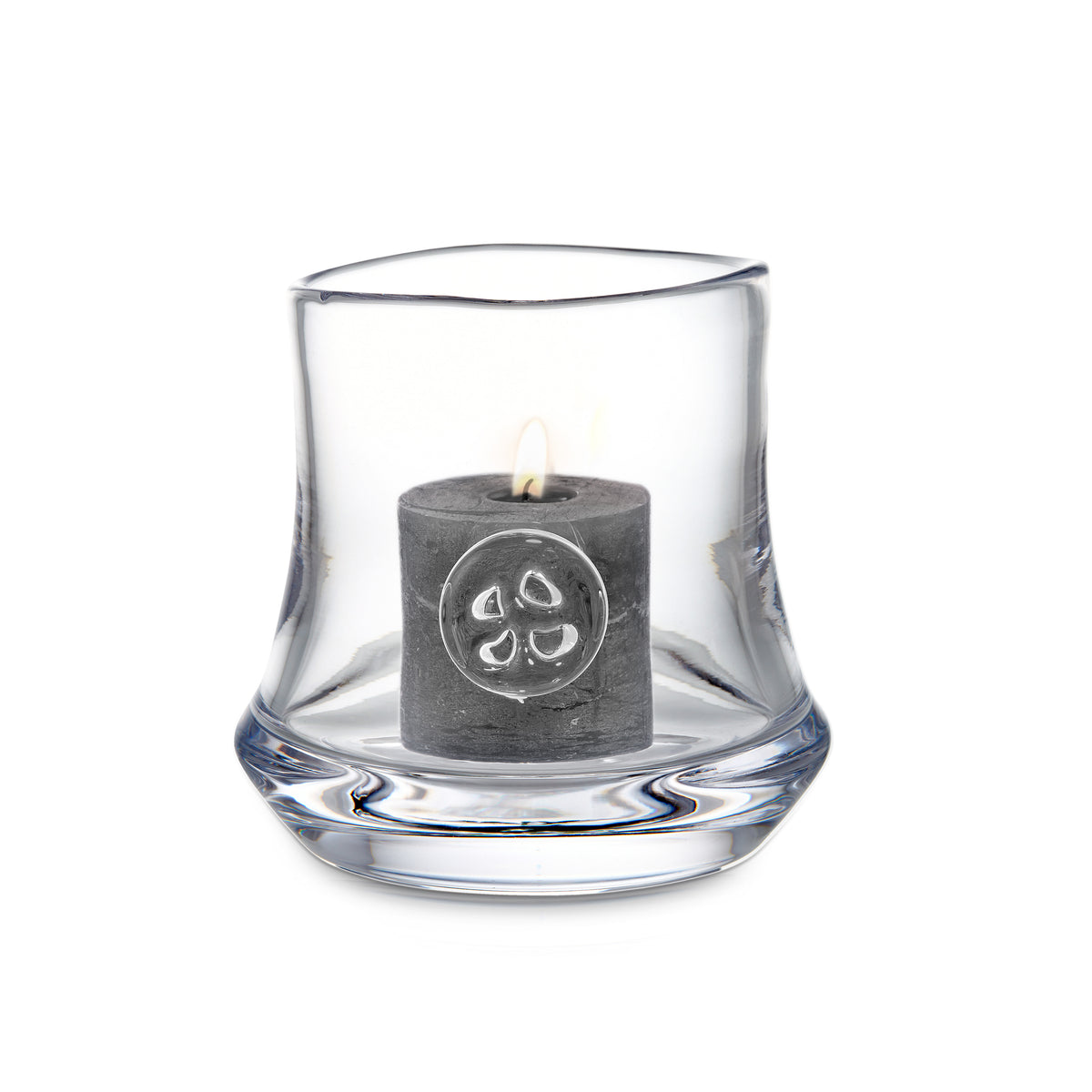 Clear glass hurricane with curved wavy sides holding a lit gray pillar candle with decorative symbol.