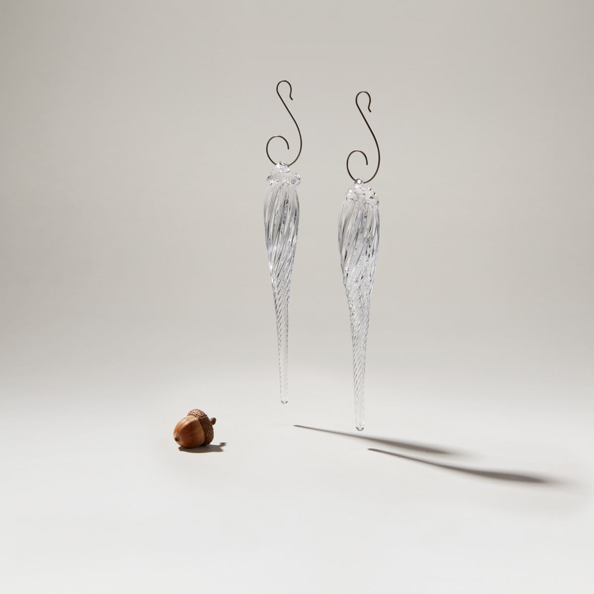 Two clear glass icicle ornaments with metal hooks and textured surfaces.