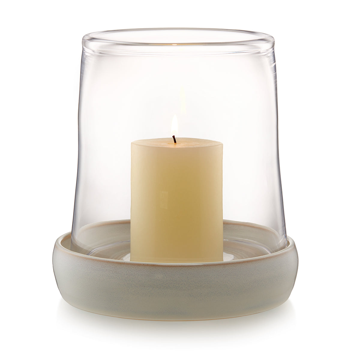Clear glass hurricane with cream-colored pillar candle and textured beige ceramic base.