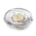 Clear glass tealight holder with cream-colored candle and lit flame, circular textured design.