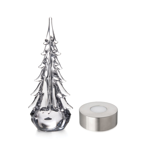 Clear glass evergreen tree with pointed branches and rounded base next to silver cylindrical gift box.