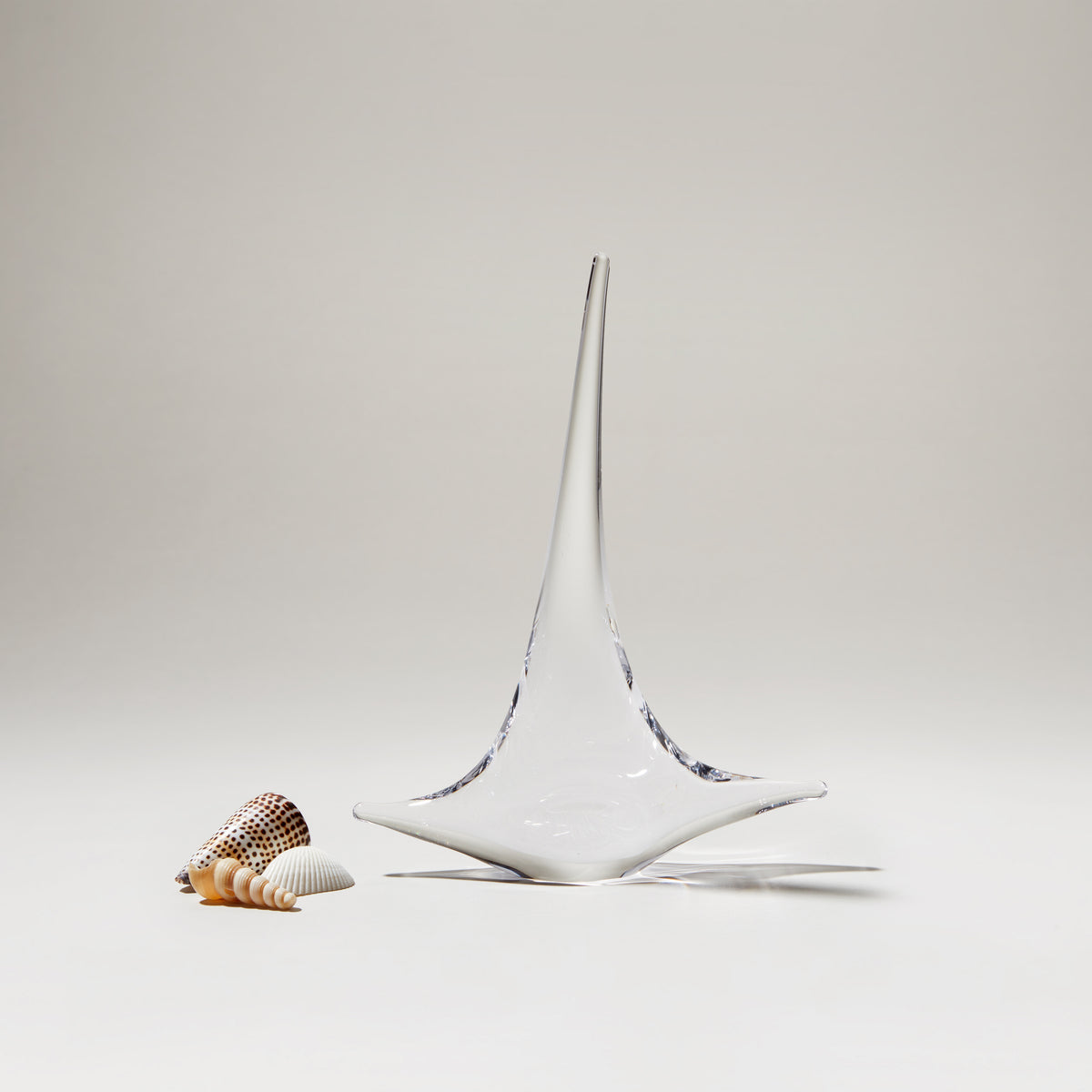 White ceramic sailboat with pointed mast and blue accents, displayed next to small shells on neutral background.