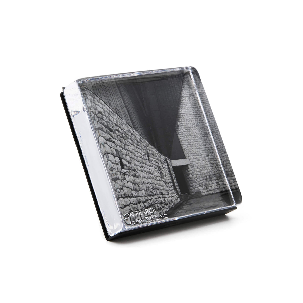 Clear acrylic square photo block with black and white brick wall photograph inside, displayed at an angle.