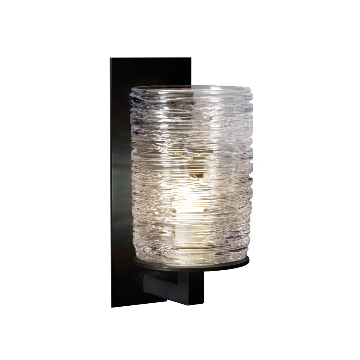 Black wall sconce with textured clear glass cylindrical shade lit from within.