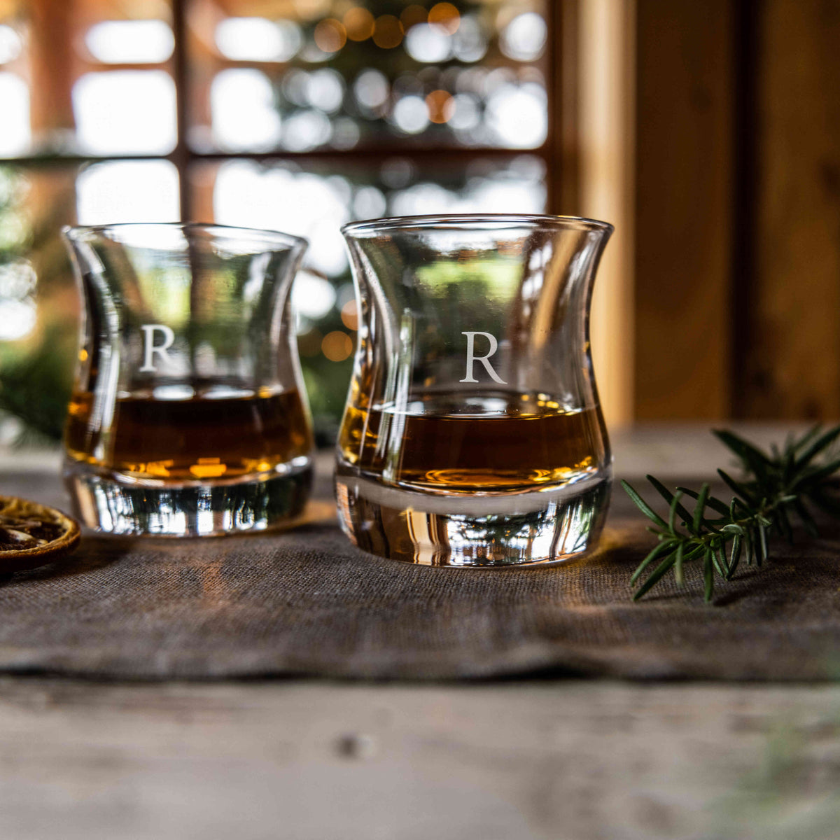Two clear double old-fashioned glasses with "R" monogram, filled with amber liquid and ice.