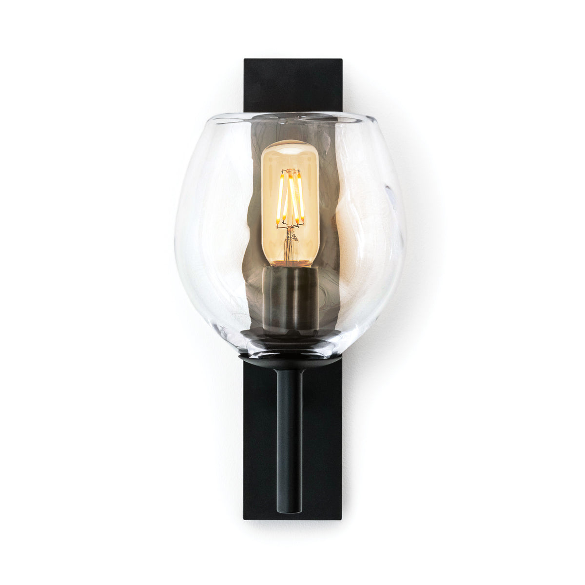 Black wall sconce with clear globe shade and lit Edison-style filament bulb.