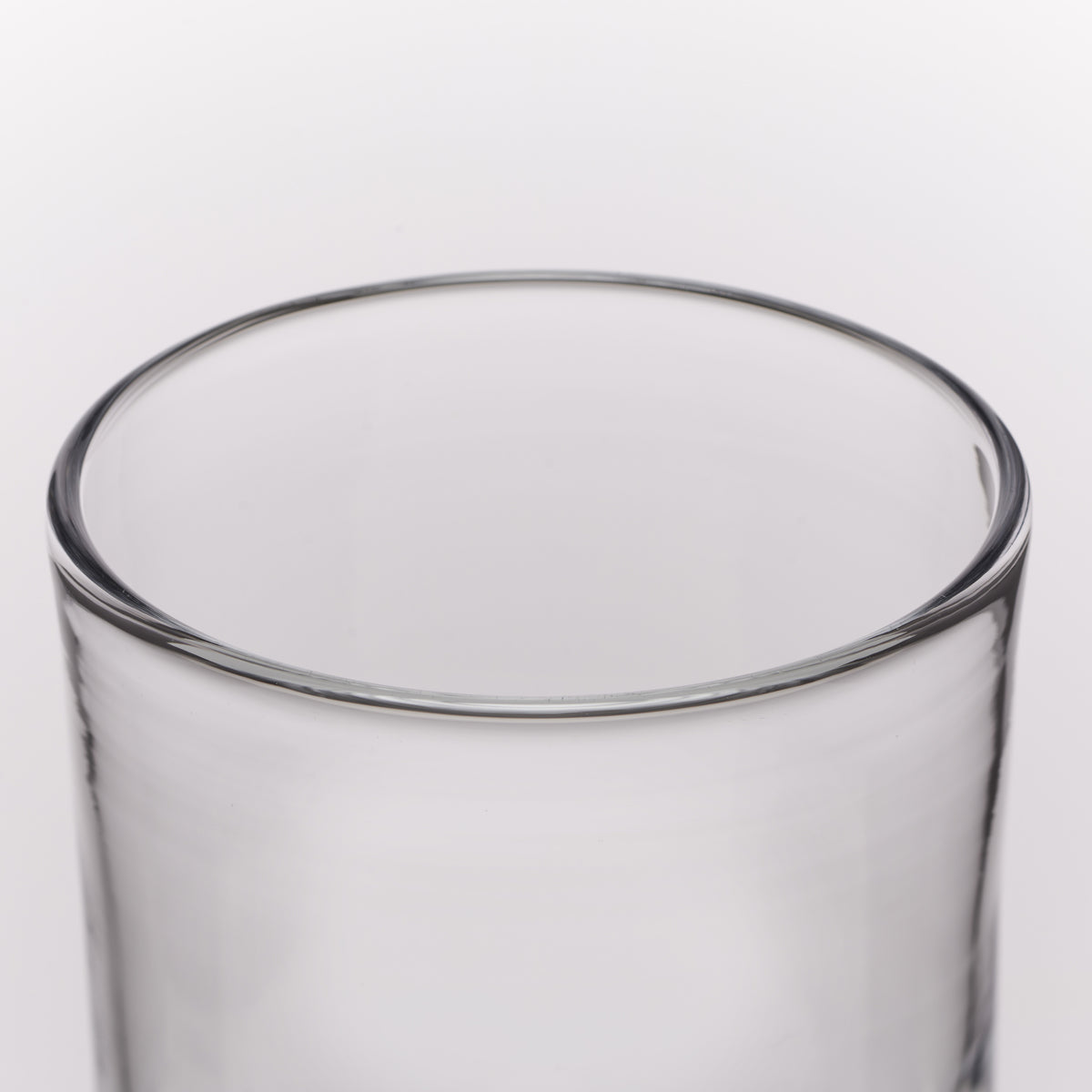 Close-up of a clear glass tumbler showing the rim and upper body against a light gray background.