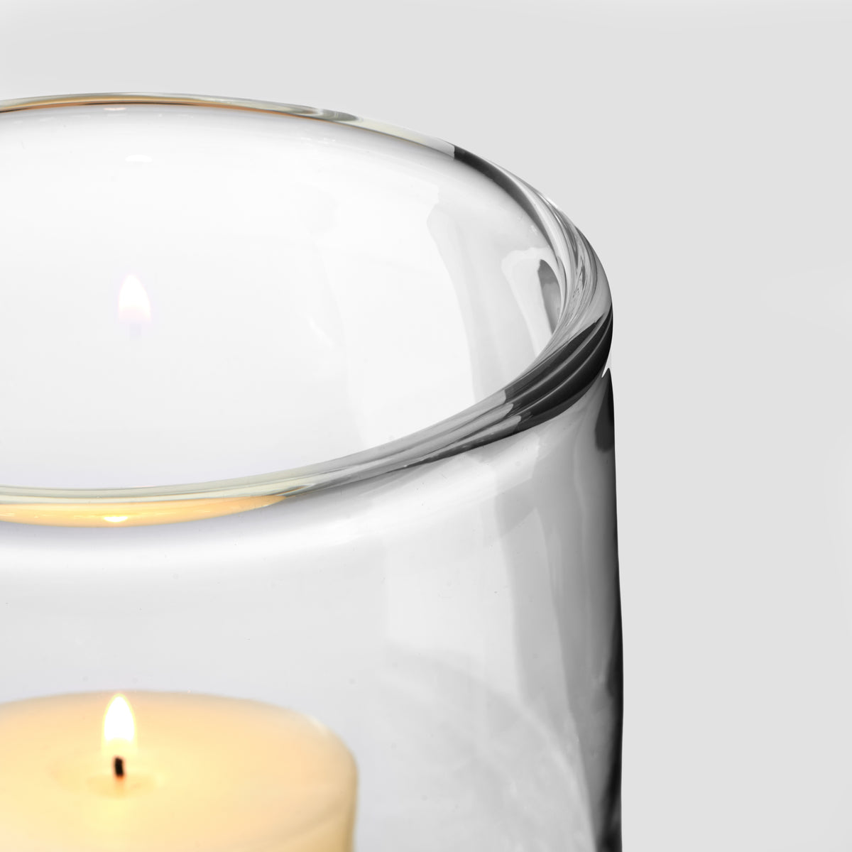 Clear glass hurricane with mixed media rim in metallic tones, lit candle visible inside.