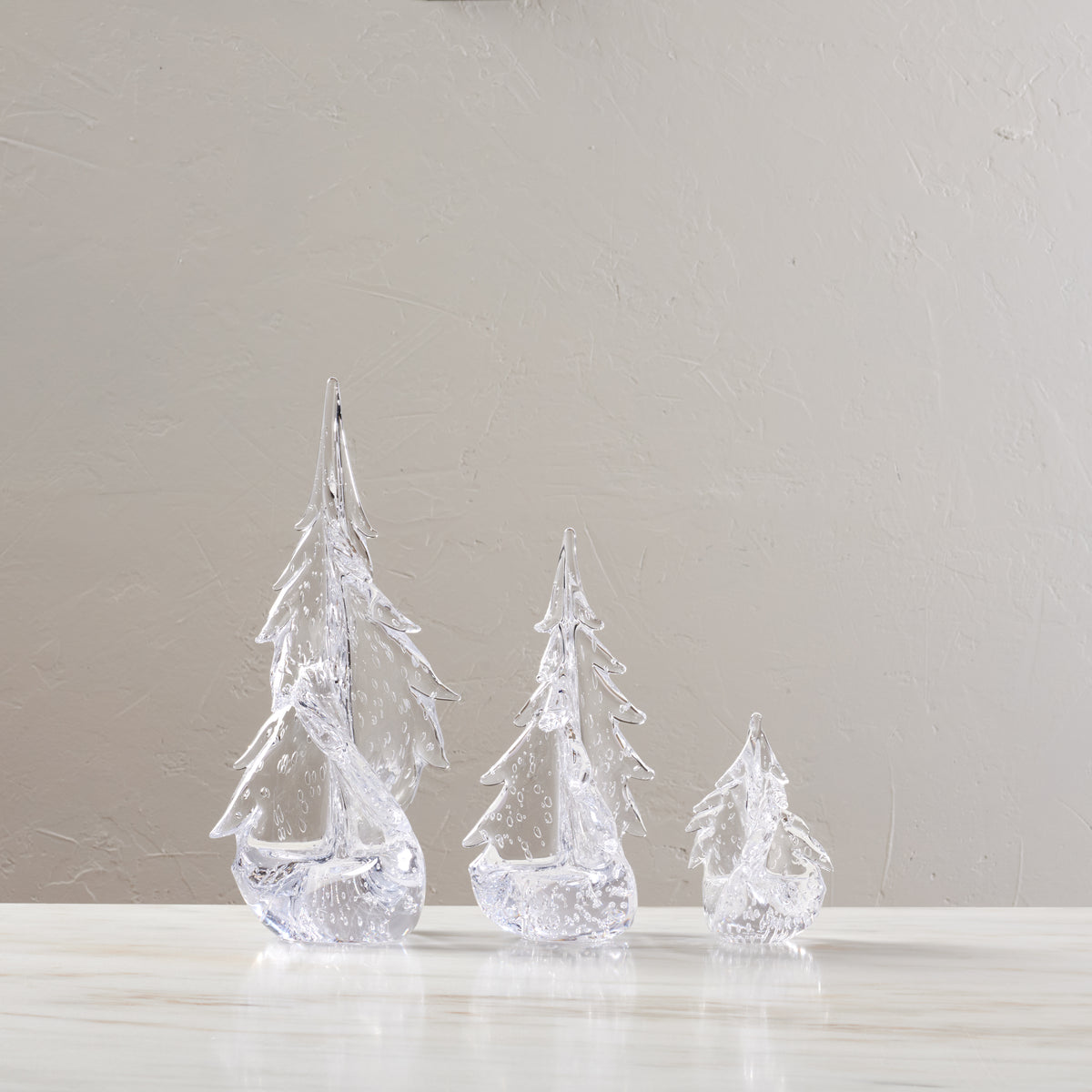 Three clear glass tree-shaped decorations with twisted, layered designs in decreasing sizes.