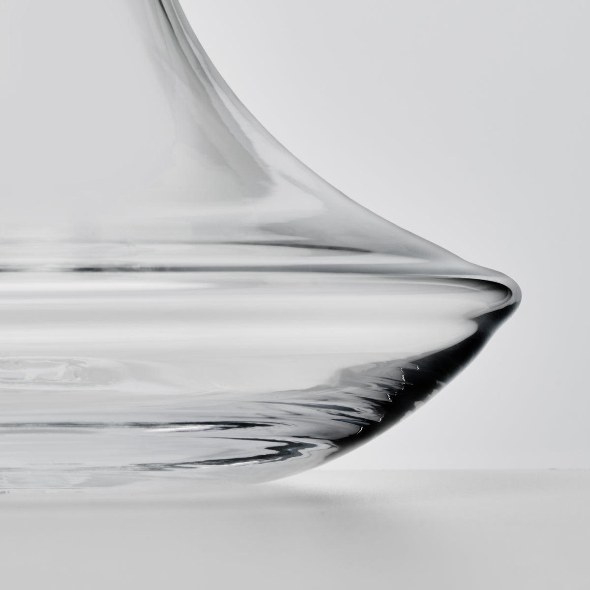 Clear glass wine decanter with curved spout and wide base, shown in profile against white background.