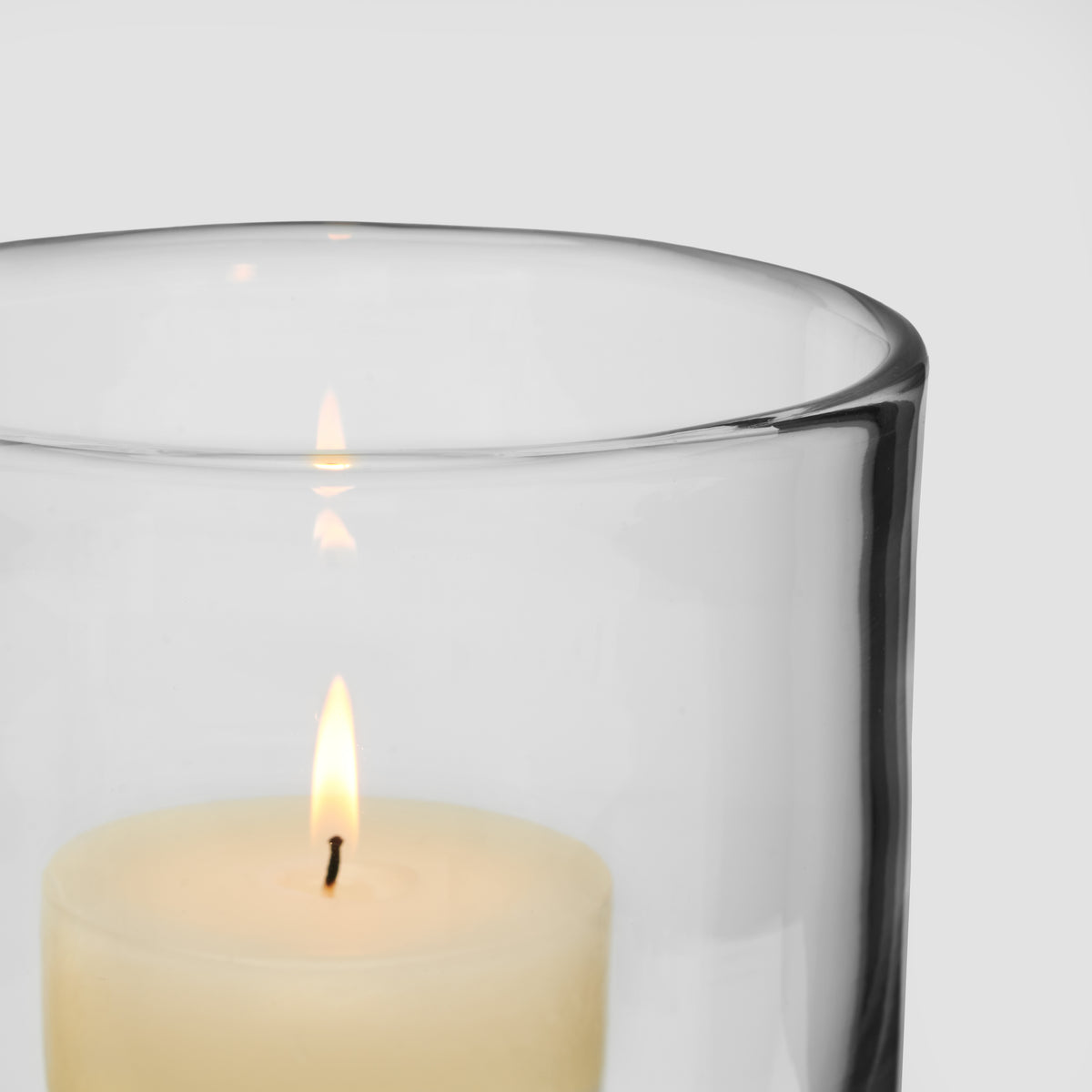 Large clear glass hurricane candle holder with burning cream-colored pillar candle inside.