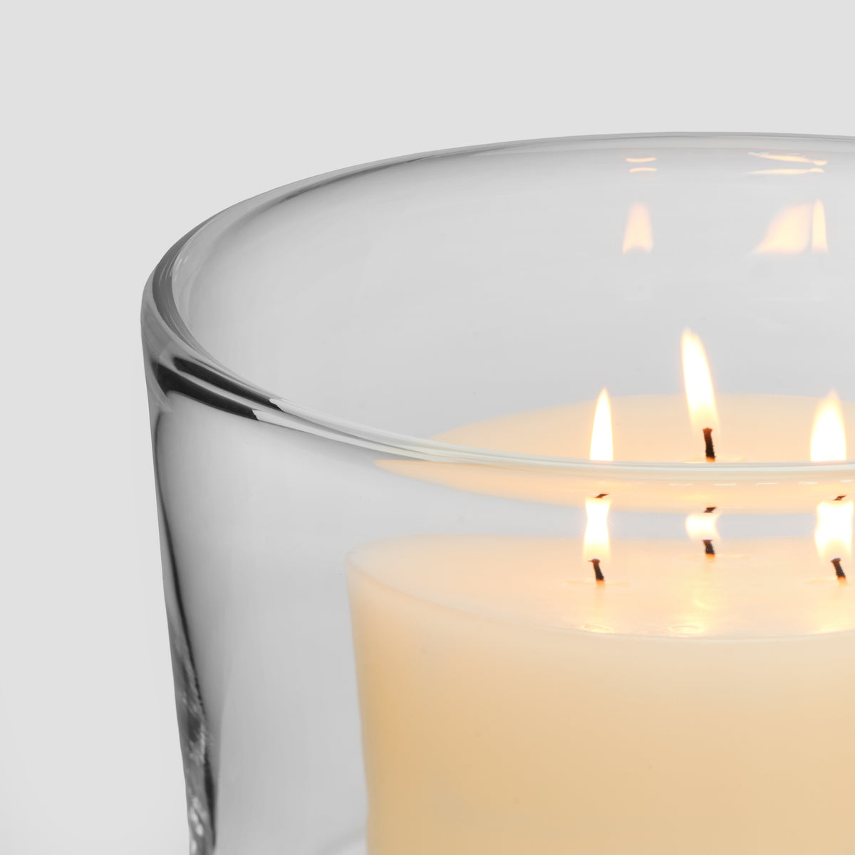 Glass hurricane candleholder with cream-colored candle and multiple lit wicks inside.