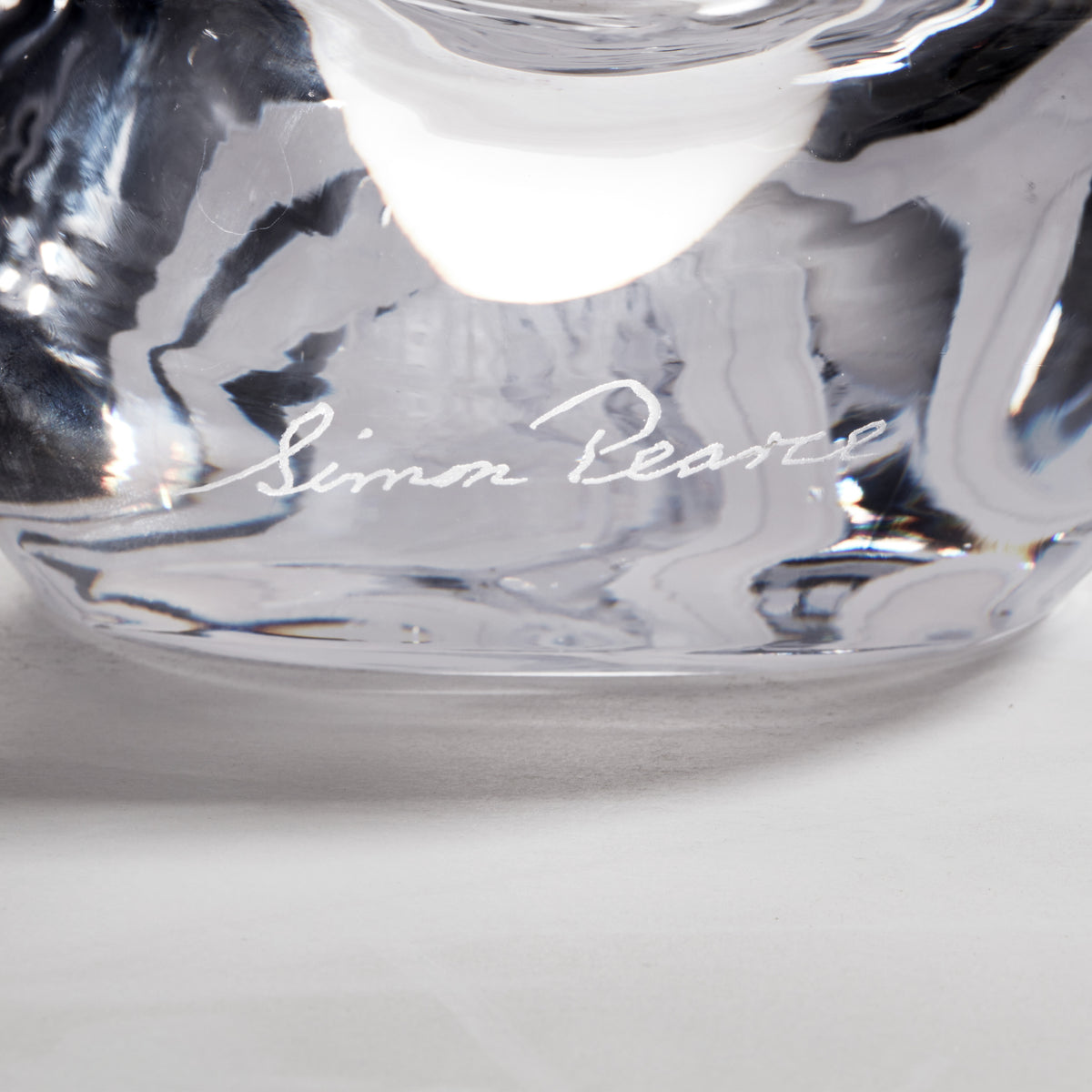 Clear glass ornament with black branch silhouettes and "Lonna Pearce" signature engraved on surface.