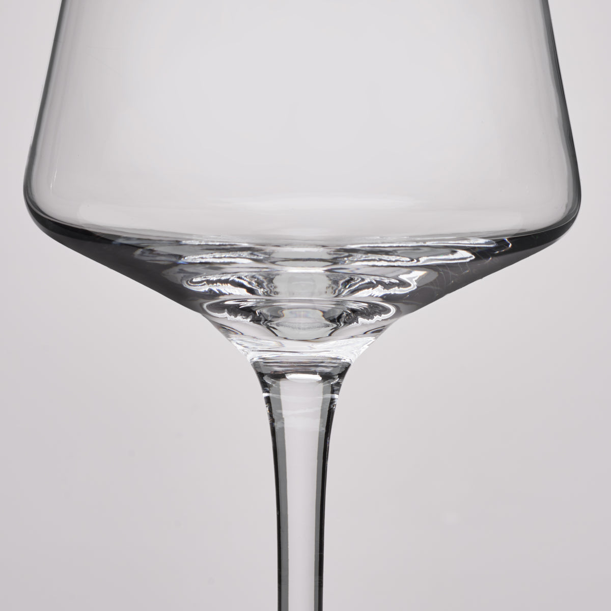 A close-up studio shot of a clear glass wine glass against a light gray background.