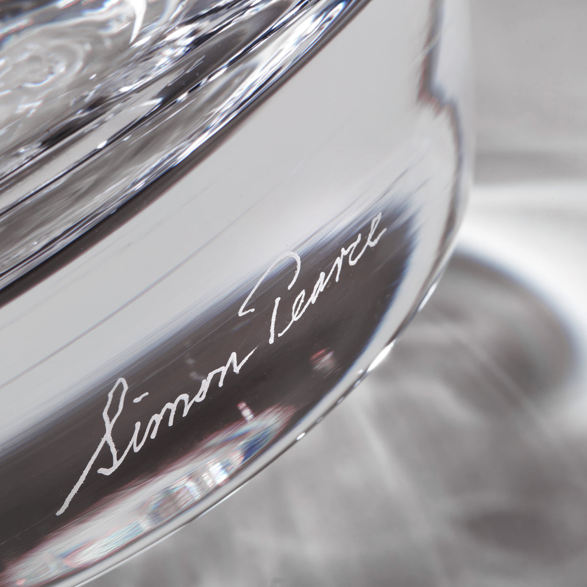 Clear glass hurricane with "Simon Pearce" signature etched on dark band, shown in close-up detail.