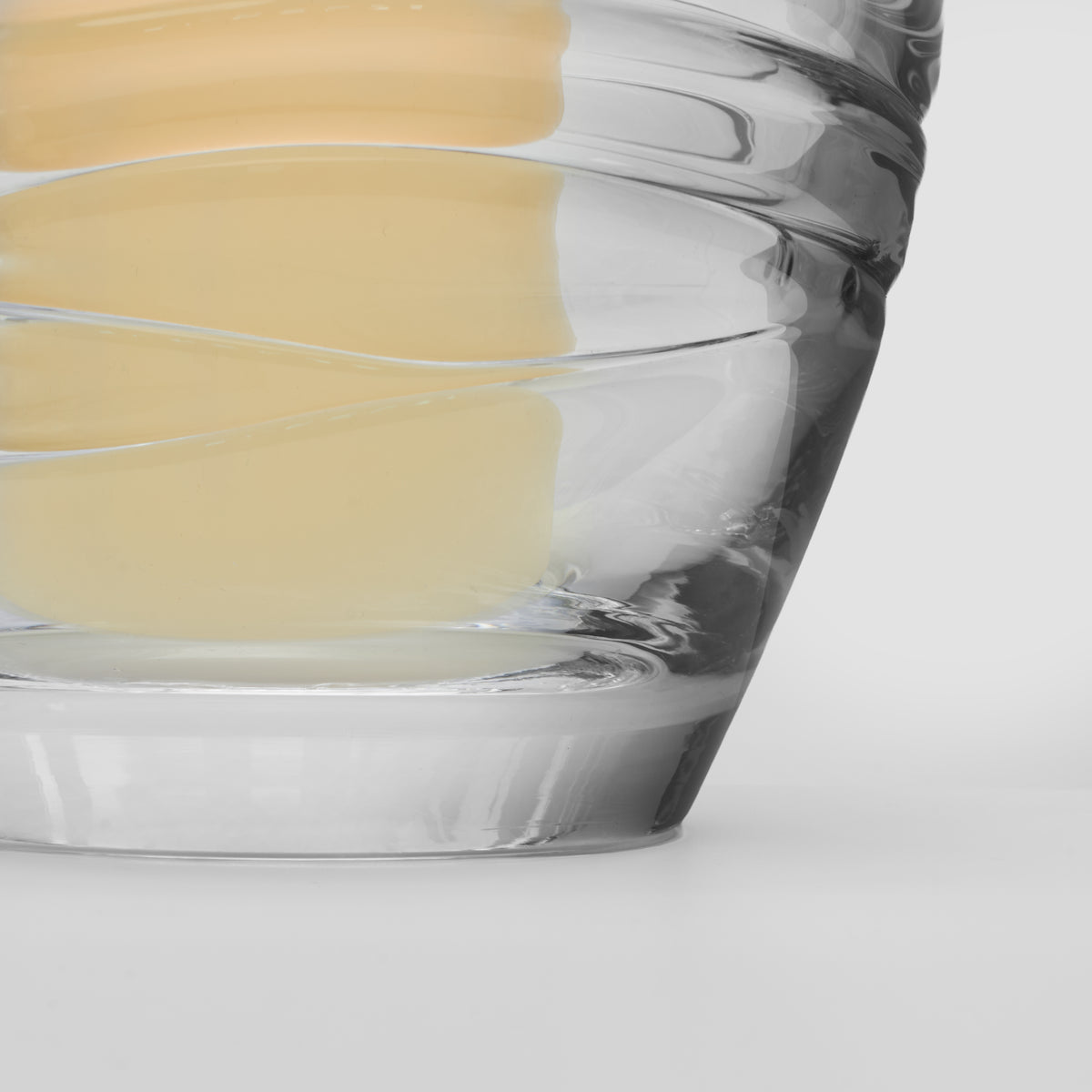 Clear glass hurricane with pale yellow candle inside, shown from side angle against white background.