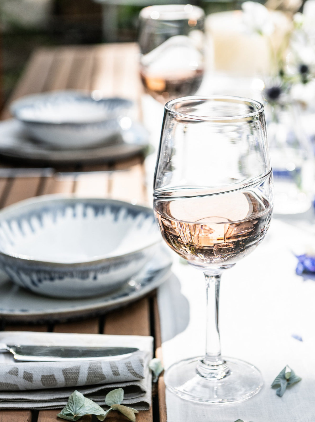 Glass of red wine on a formal dining table setting with plates and place settings.