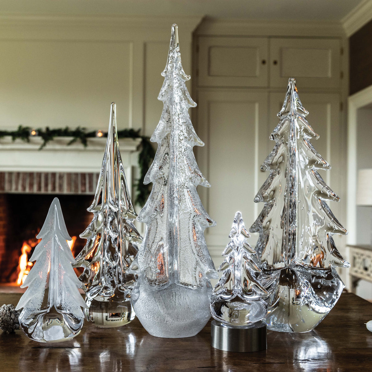Five clear glass tree figurines in varying heights with frosted and textured finishes, displayed on a dark surface.