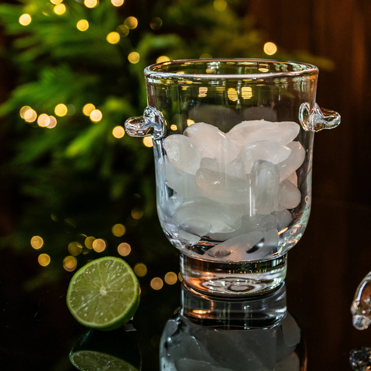 Clear glass ice bucket filled with ice cubes, featuring two handles and a footed base.
