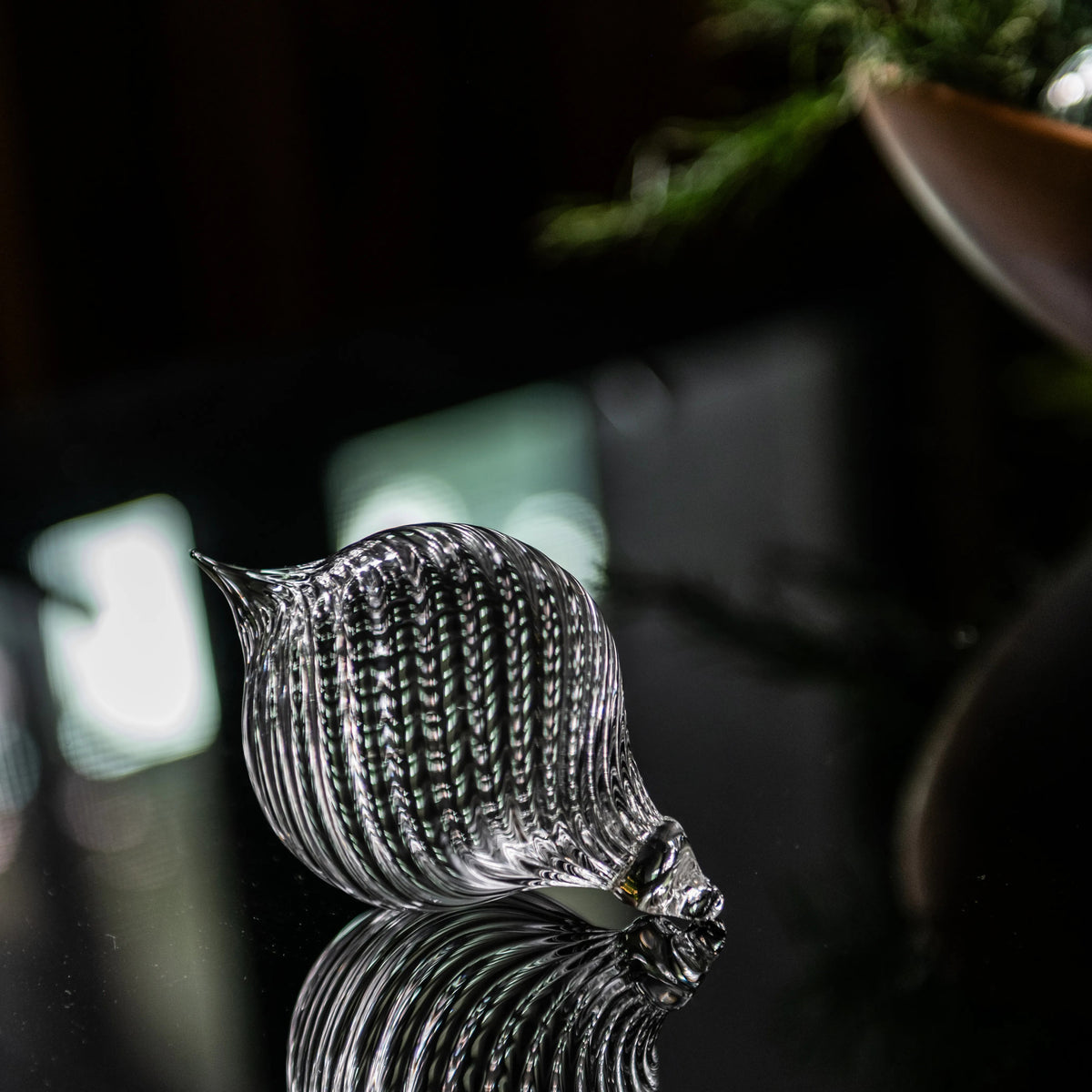 Clear glass finial ornament with ribbed texture and pointed top, displayed against dark background.