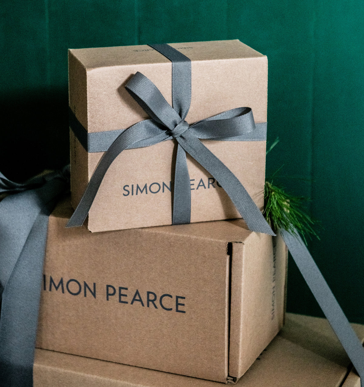 Two Simon Pearce kraft gift boxes stacked, the top one tied with a gray grosgrain ribbon bow