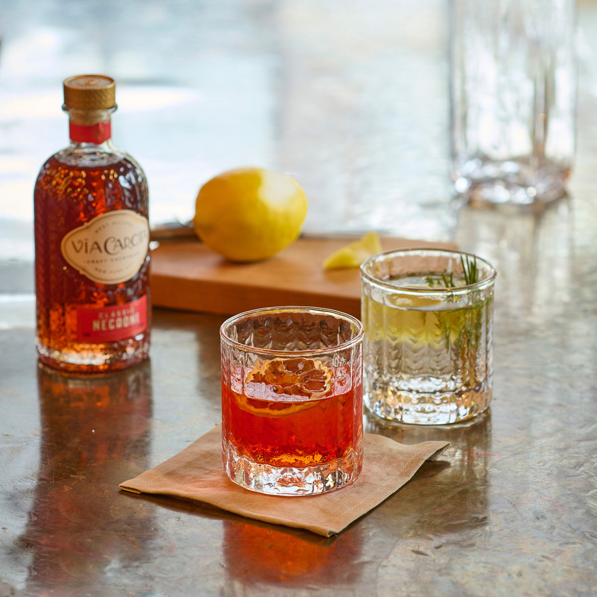 Two clear lowball glasses with textured pattern, one filled with red liquid and one with amber liquid, displayed with a bottl