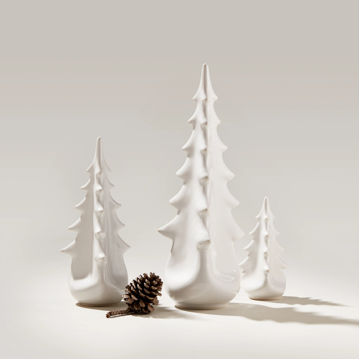 White ceramic evergreen tree figurines in three graduated sizes with a pinecone.