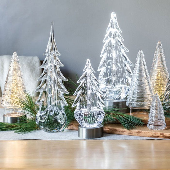 Illuminated glass and metallic decorative trees in various heights with frosted and clear finishes on wooden base.