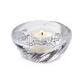 Clear glass shell-shaped tealight holder with lit cream candle inside.