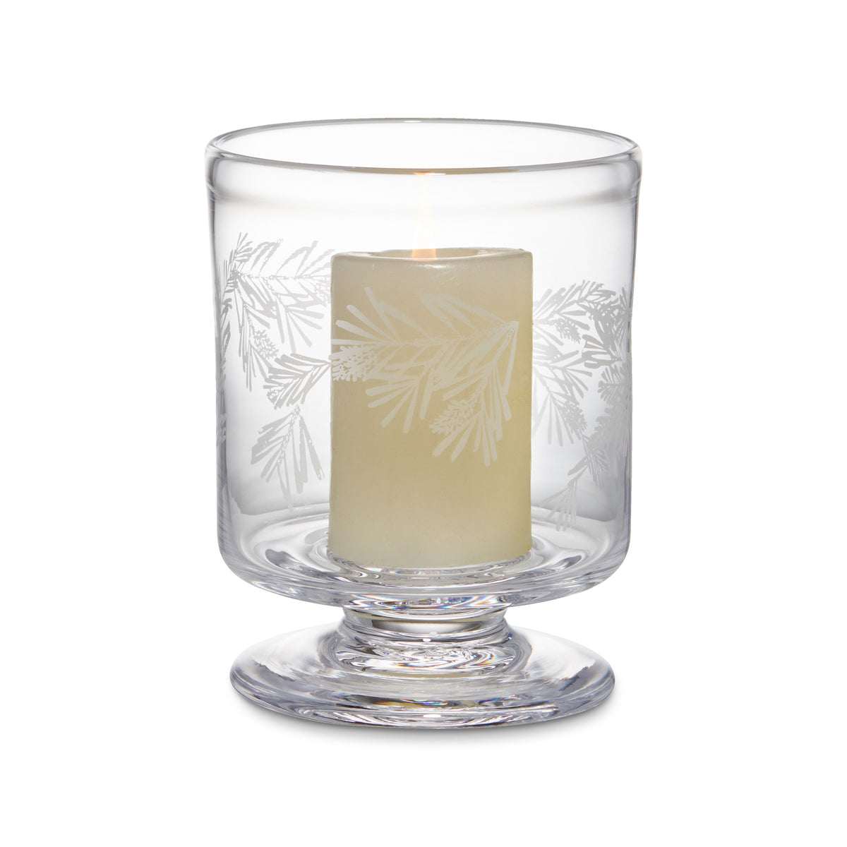 Clear glass hurricane with engraved pine branch design and cream-colored pillar candle inside.