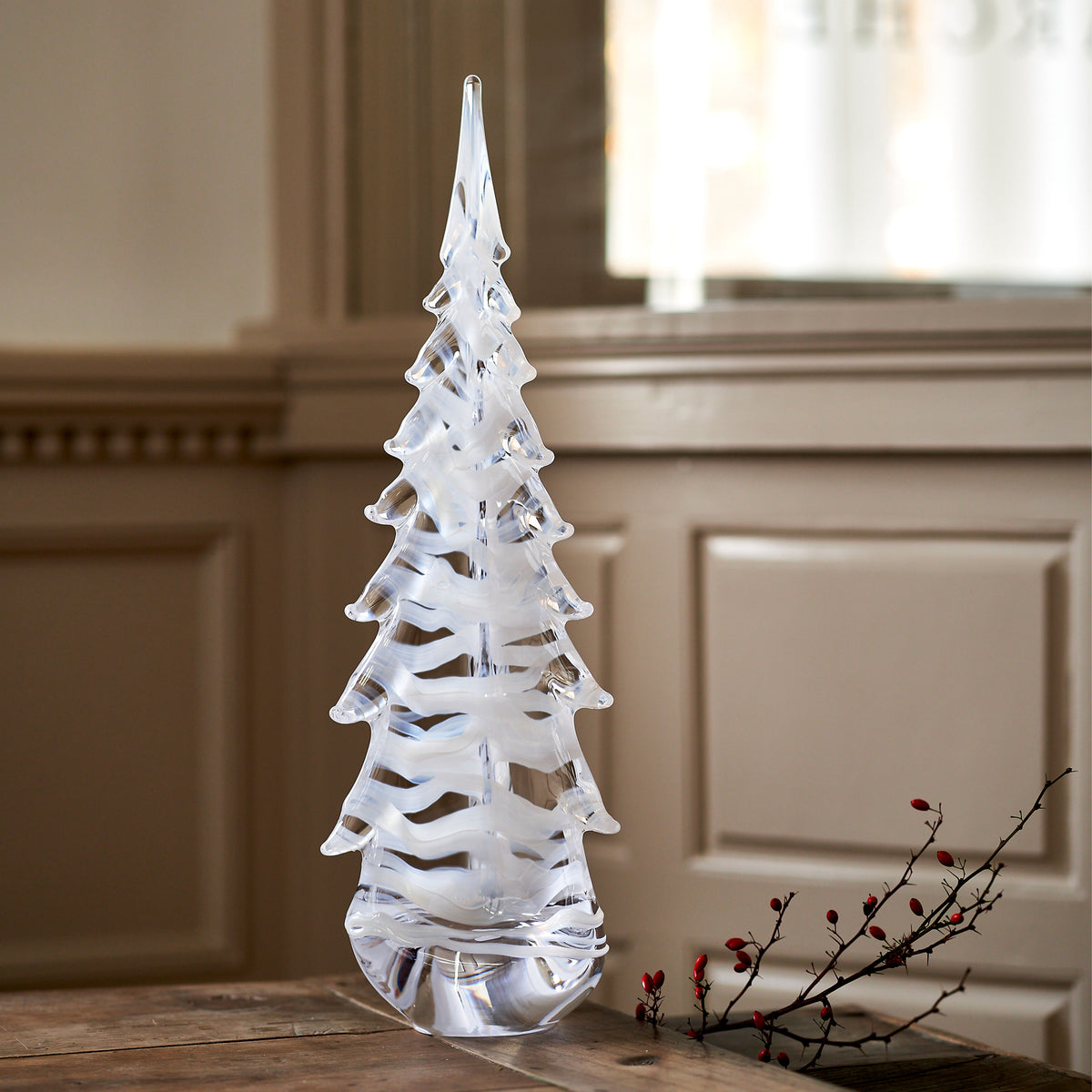Clear glass evergreen tree figurine with layered branches and pointed top on wooden surface.