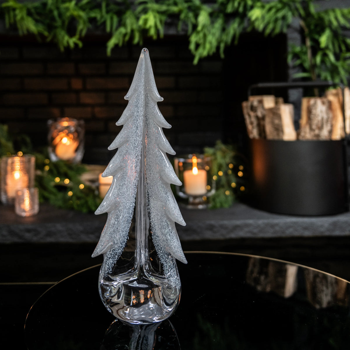 Frosted glass evergreen tree decoration with layered branches and clear base on dark surface.