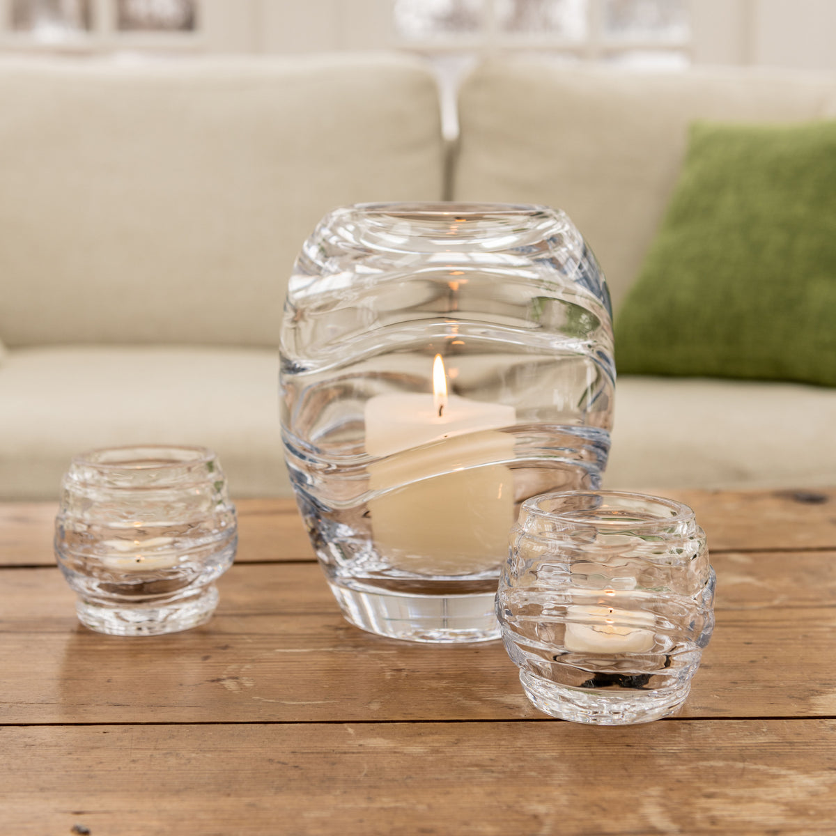 Two clear glass tealight holders with wavy ridged design, one larger and two smaller, each containing a lit cream-colored can