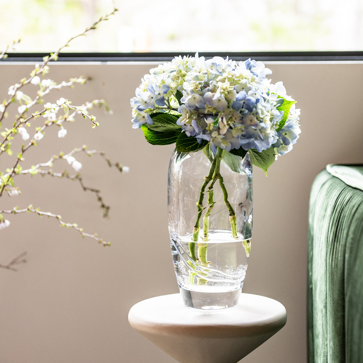 Clear glass vase with blue and white hydrangea flowers and green stems in water.