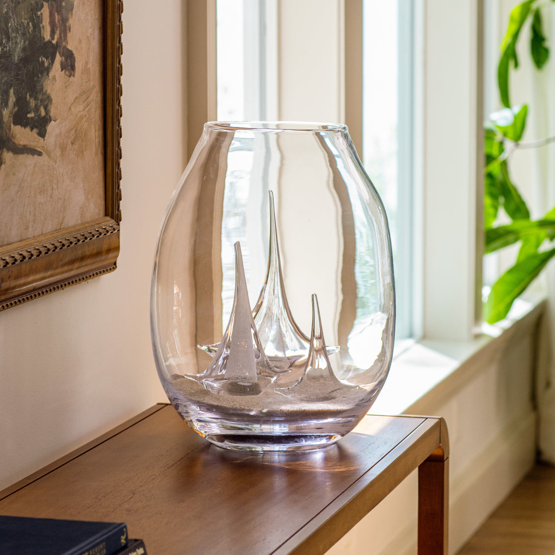 Clear glass vase with etched sailboat design, displayed on wooden table near window.