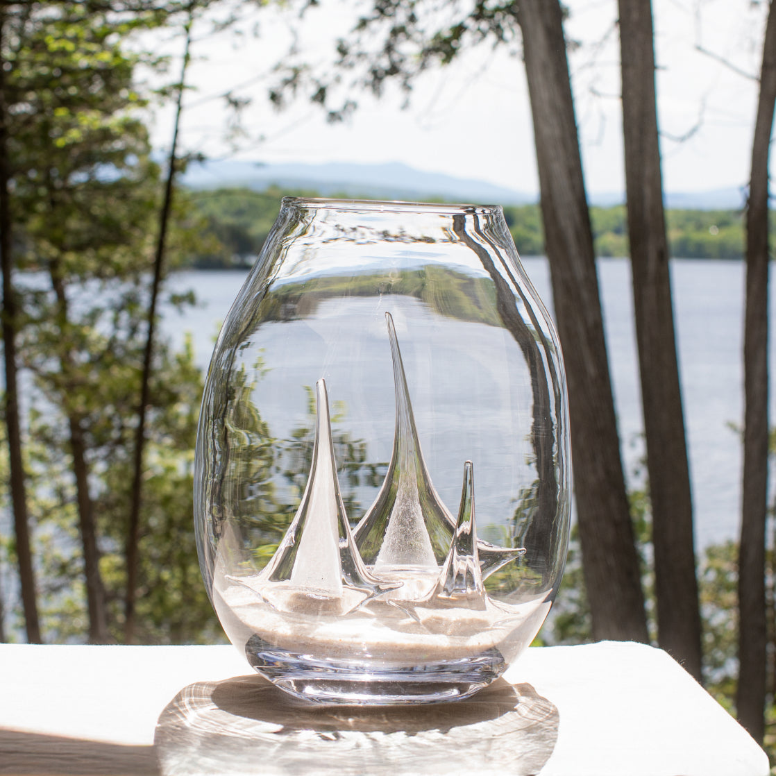 Clear glass globe with etched sailboat design inside, displayed outdoors by a lake.